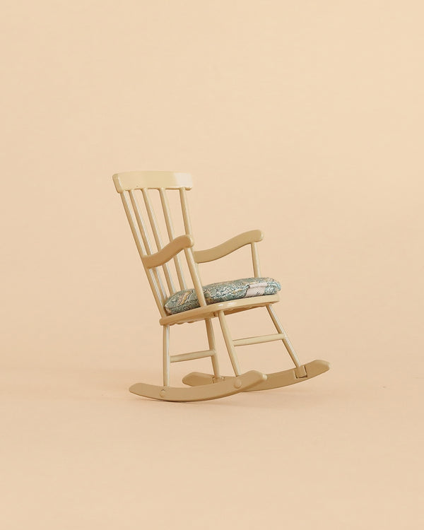 A light wooden “Rocking Chair, Mouse - Wheat” with a floral-patterned cushion sits on a beige background.
