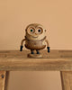 The Boyhood Minion Bob wooden figurine, featuring mismatched eyes and a "BOB" label on its base, stands on a wooden table with a plain beige background.