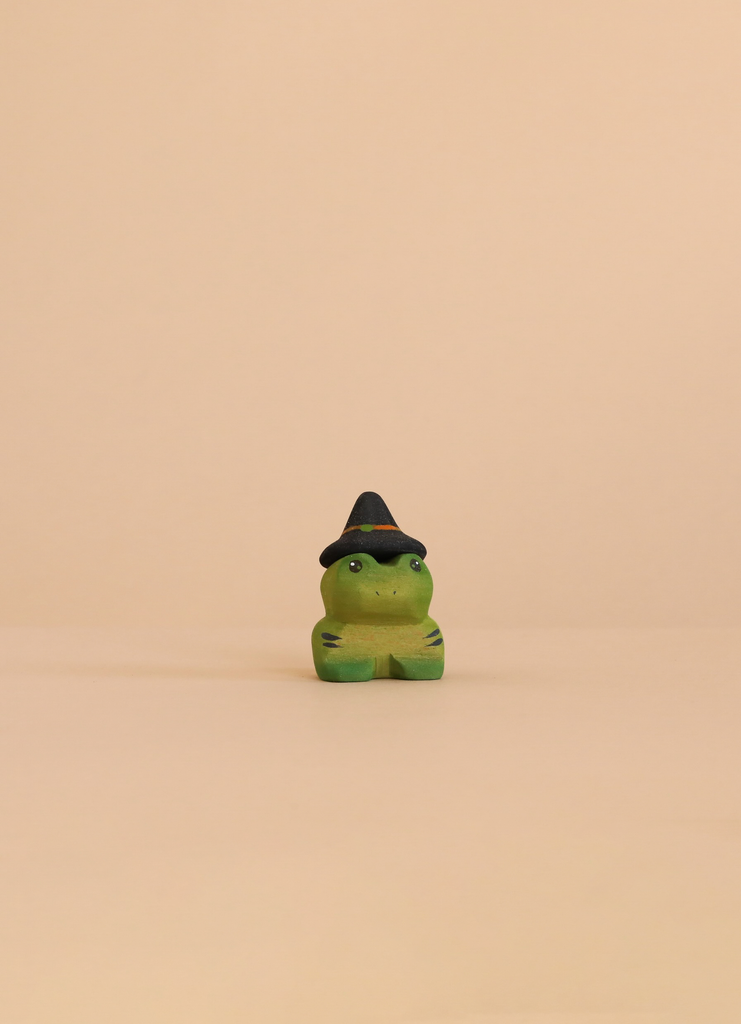 A small Bumbu Handmade Wooden Halloween Friends Set wooden frog figurine wearing a black witch’s hat with an orange band, perfect for Waldorf toys.