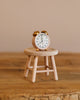 Small pink alarm clock with gold bells sitting on a miniature wooden stool inside the Maileg Grandma’s Living Room Set.