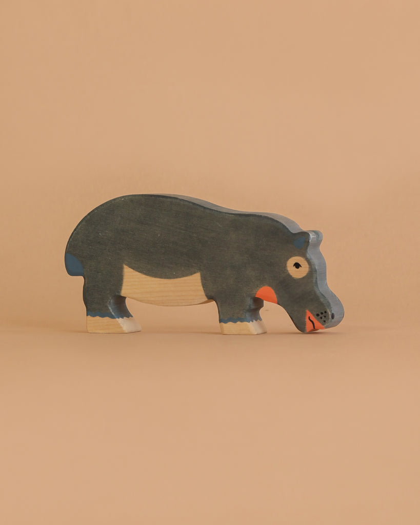 A Holztiger Hippopotamus, Feeding figure—handcrafted from wood and painted in dark gray, white, and orange—stands on a light beige background.