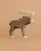 A handcrafted Holztiger Elk figure, featuring a painted gray body and white antlers, stands upright against a plain beige background.