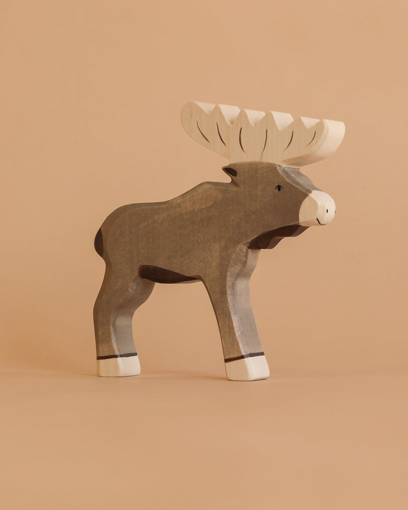 A handcrafted Holztiger Elk figure, featuring a painted gray body and white antlers, stands upright against a plain beige background.