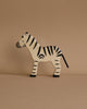 A wooden zebra from the Holztiger Handmade Wooden Safari Animals Set, with black stripes, stands against a plain beige background, showcasing the charm of handmade wooden toys.