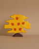 A handcrafted wood tree figure with a bright yellow canopy and orange leaves. The dark brown base complements its whimsical, playful appearance, typical of Holztiger Maple Tree figures. Set against a plain beige background, this charming piece adds delightful play value to any setting.