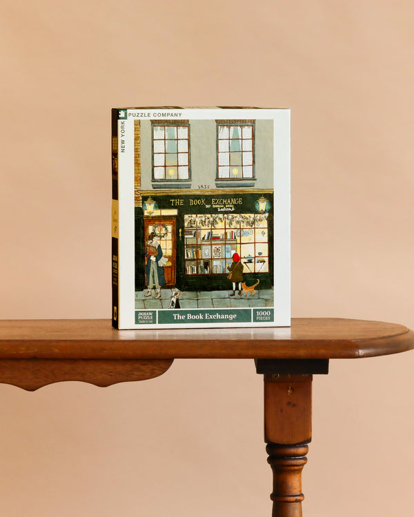 The Book Exchange - 1000 Piece Jigsaw Puzzle features a cozy bookshop scene with people browsing inside and out—an ideal holiday gift for book lovers, displayed on a wooden table against a beige background.
