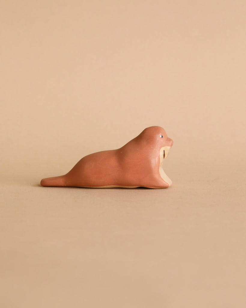 The Handmade Wooden Walrus, brown with simple features, rests on a plain matching background. Crafted like a timeless toy with child-safe paint, it captures the essence of natural beauty artfully in every detail.