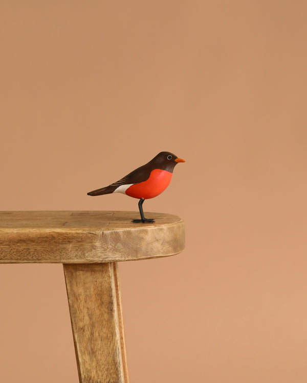 The Hand Carved Ornament - Mini Robin Bird - 3"H features a red belly and brown wings, perched on the edge of a stool against a plain beige background.