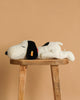 The Steiff XL Snoopy Lying Down 16" toy rests on its side atop a wooden stool set against a plain beige background.