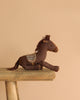 The Maileg Cowboy Set, featuring a brown plush horse with a patterned saddle, rests on a wooden bench against a simple beige backdrop.