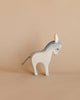 A light grey and white donkey from the Ostheimer Handmade Wooden Farm Animals Set stands on a beige surface with a matching background.