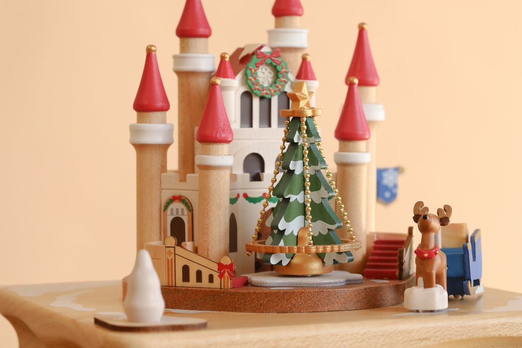 Christmas Castle Music Box shaped like a castle with red-roofed towers, a central Christmas tree with golden garland, and a small reindeer figure.