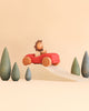 A wooden lion figurine from the Sabo Concept First Journey set drives a red toy car over a wooden ramp, surrounded by small green toy trees designed to develop coordination skills.