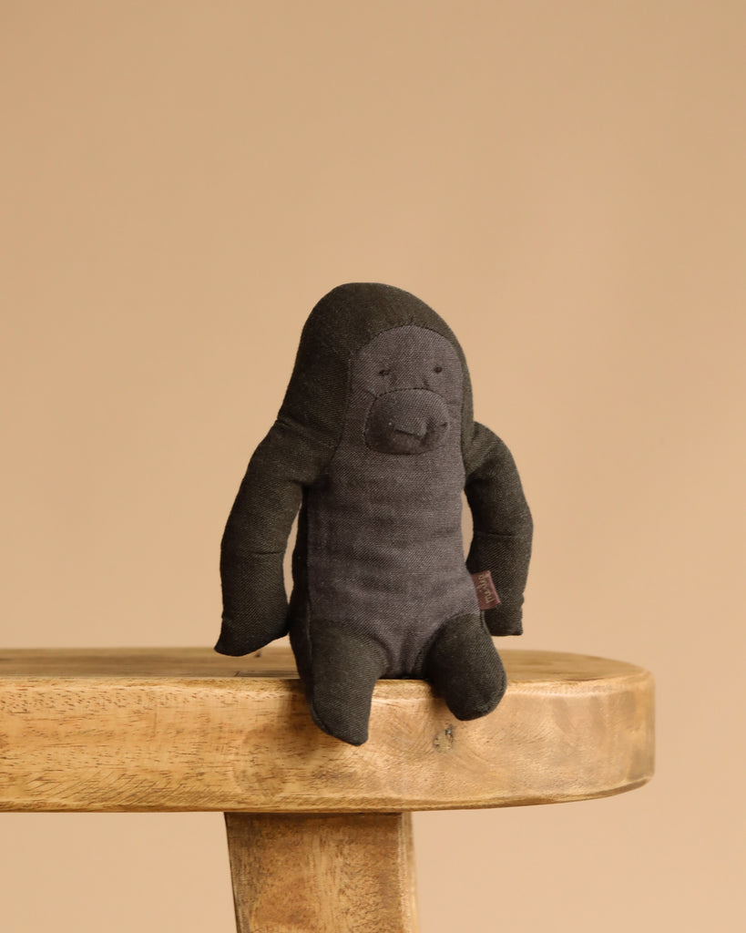 The Maileg Gorilla, Mini is a handmade stuffed toy crafted from soft fabric, sitting on a wooden stool against a beige background—perfect for adding to your Safari friends collection.