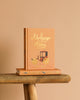 A peach Collector's Edition hardcover of "Northanger Abbey" sits upright on a rustic wooden surface, adorned with gold lettering and a carriage illustration, resting atop another book.