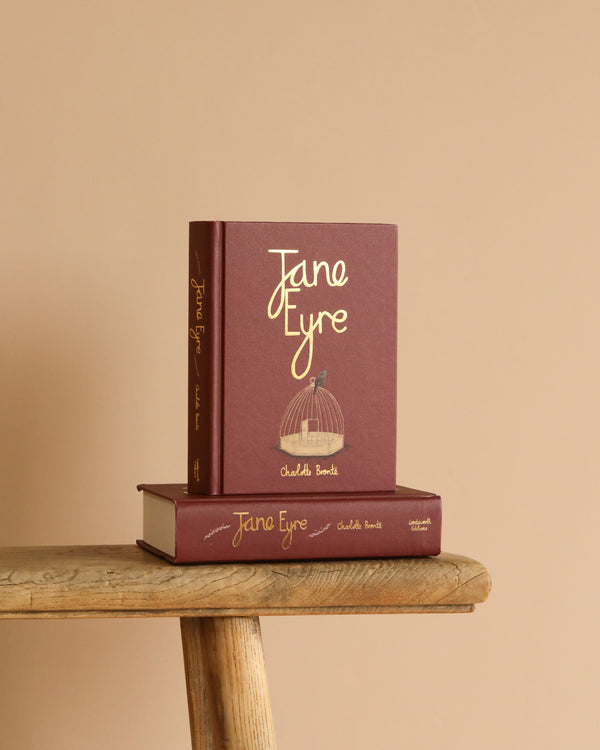 Two Jane Eyre | Brontë | Collector's Edition | Hardcover books, one upright and one flat, with maroon covers and gold text, are displayed on a wooden bench against a beige background.
