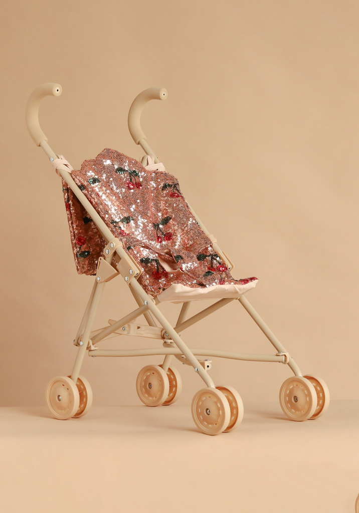 Konges Sloejd Sparkly Doll Stroller - Cherry Sequin with double wheels, a light beige frame, and a seat made of washable fabric covered in pink sequins with a cherry pattern.