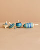 The Mader Spinning Top Champion Learning Set - Ice features five fun tops in various shapes and sizes with blue and green stripes, arranged upright and on their sides on a beige surface—ideal for beginner to advanced spinners.