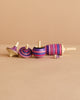 The Mader Spinning Top Champion Learning Set - Lilac features four fun tops in purple, pink, and blue stripes, including one tiny top. All meet toy safety standards and add playful color to any collection on a plain beige surface.