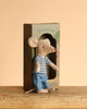 A Maileg LouisMax Mouse - Big Brother in a striped shirt and blue pants sits before a decoration box, perched on a wooden surface against a beige background, inviting imaginative journeys.