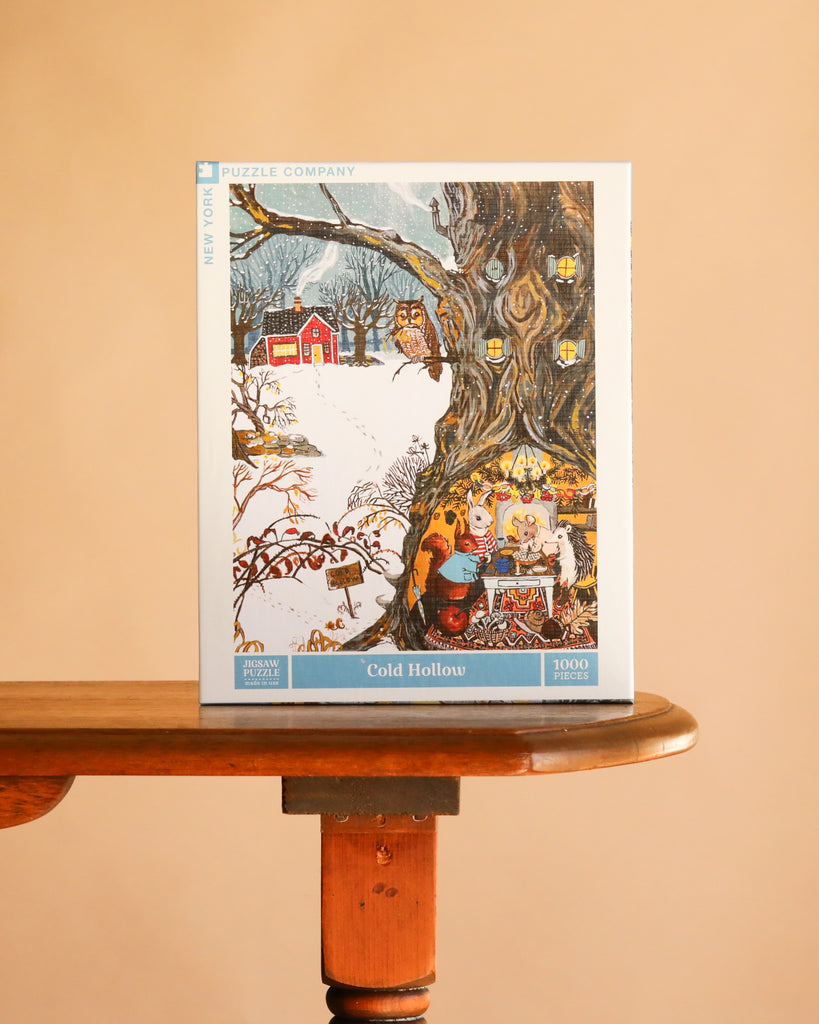 The Cold Hollow - 1000 Piece Jigsaw Puzzle box features an owl perched on a snowy tree, with animals having tea inside a hollow trunk and a red cabin in the background.