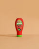 The Erzi Ketchup Pretend Food is a realistic toy bottle with a green cap, standing upright on a beige surface. Non-toxic and ideal for store or kitchen play, it features a tomato label reading "Bio Ketchup.