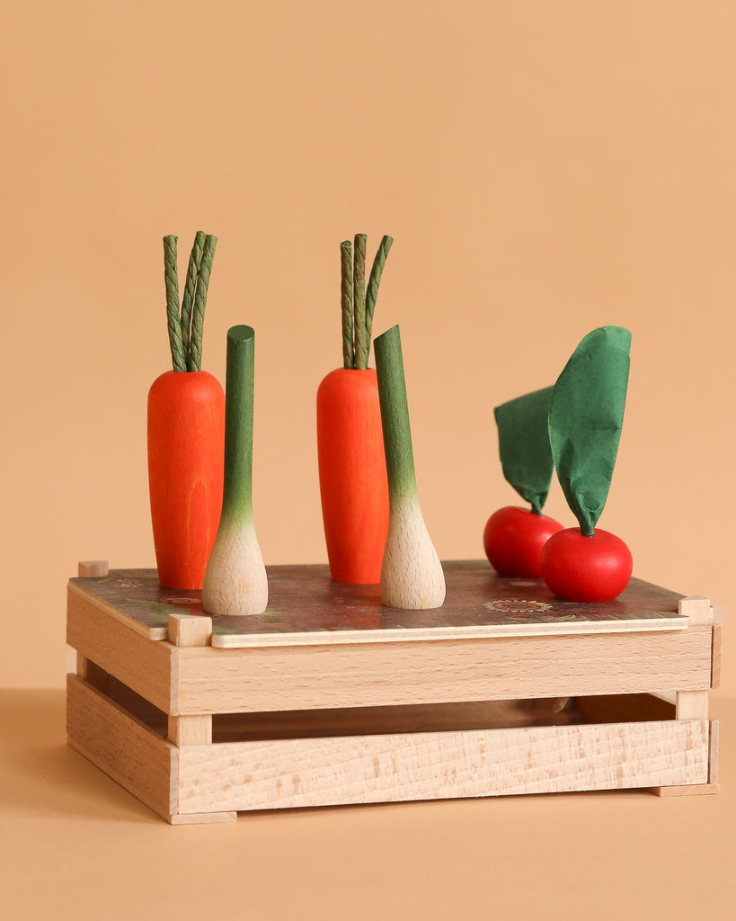 The Erzi Vegetable Patch Garden Set includes toy veggies—two orange carrots, two white-and-green scallions, two red tomatoes, and two green leaves—in a wooden crate, evoking the charm of an Erzi garden.