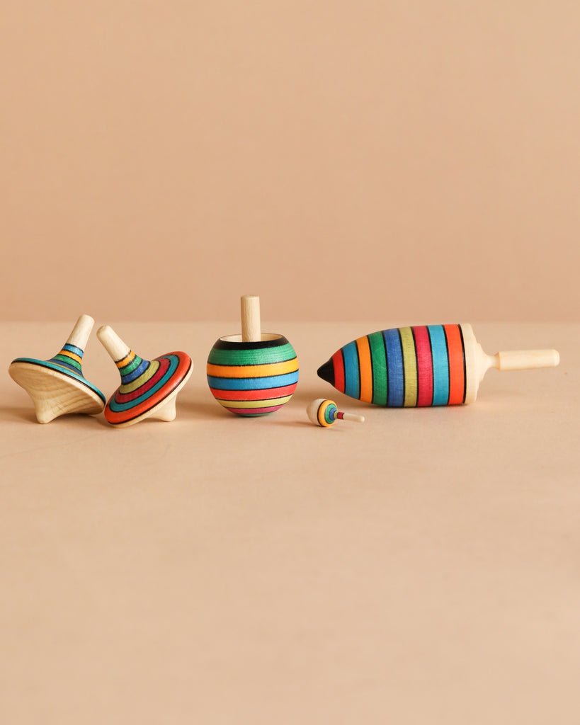 The Mader Spinning Top Champion Learning Set - Striped features five colorful, striped tops in various shapes and sizes—including an elongated one—neatly arranged on a beige surface; all meet toy safety standards to reduce choking hazard risks.