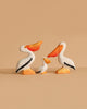 The Bumbu Handmade Wooden Pelicans Family Set features three sustainable wooden pelicans—two large and one small—painted white with orange beaks, feet, and black wings. Perfect for Montessori play and displayed against a beige background.