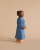 A wooden figurine of a woman stands against a beige background. The figure is carved in a simple, minimalist style and painted wearing a long blue dress. Featuring a modest hairstyle with hair pulled back and a calm expression, this piece embodies the essence of Ostheimer Mother, Blue Dress for imaginative play.