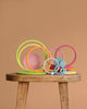 Grimm's Concentric Circles and Rings Building Set - Pastel features colorful wooden rings and discs of varying sizes, artfully stacked on a stool against a light brown backdrop, creating a playful and balanced display.