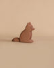 A figure from the Ostheimer Handmade Wooden Farm Animals Set—a small, brown wooden fox—rests on a beige surface with a matching beige background.
