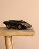 The Playforeer UFO Cannone Car in Black, styled after 70's concept cars with gold accents, is displayed on a rustic wooden stool against a plain beige background.