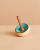 The Mader Zwirbel Spinning Top - Blue, made from Walnut and Ash with a blue interior and natural wood exterior, stands upright on a light beige surface against a beige background.