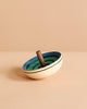 The Mader UFO Flora Spinning Top - Blue, crafted from maple wood with a dark handle and ombre green and blue concentric circles, rests on a beige surface against a coordinating beige background.
