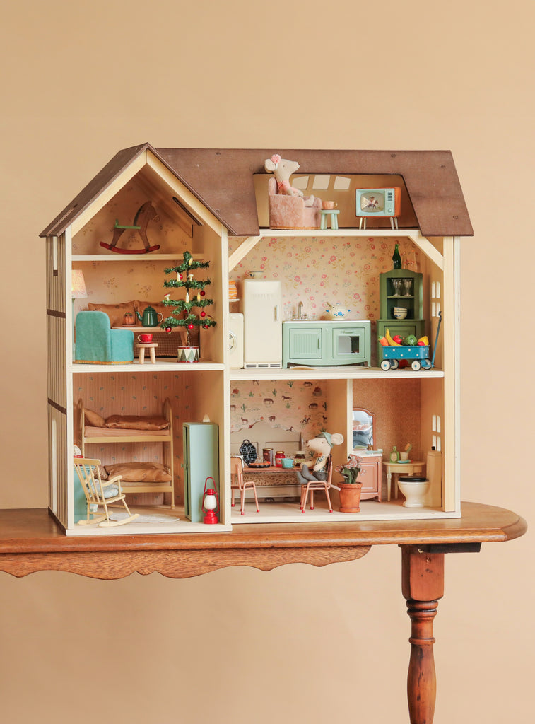 A Maileg Fully Furnished Farmhouse Set featuring a two-story farmhouse dollhouse with an attic, furnished with miniature appliances, furniture, and two mouse figures on a wooden table.