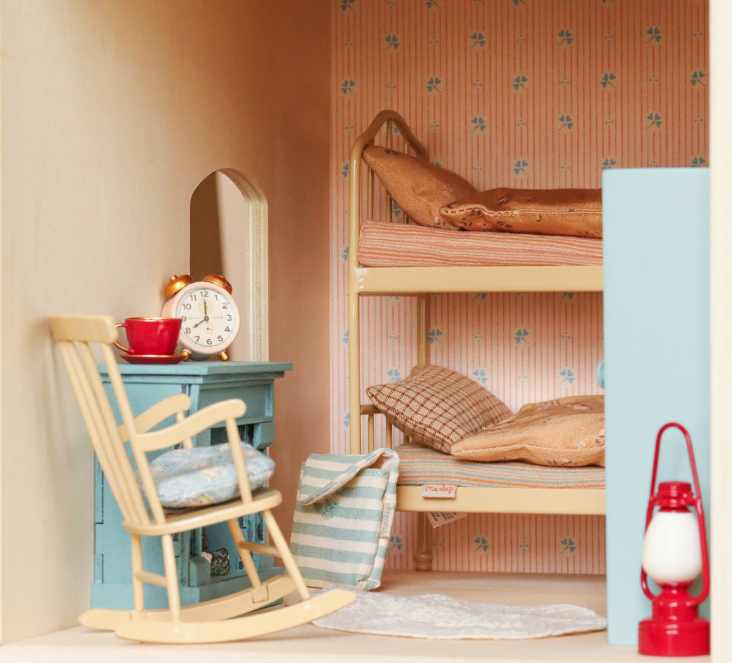 A Maileg Fully Furnished Farmhouse Set bedroom featuring a bunk bed, a blue rocking chair, a small table with an alarm clock and teacup, and a red lantern.