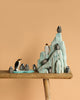 The Bumbu Handmade Wooden Penguin Set features small penguin figurines and an adult arranged by a light blue iceberg on a wooden surface, ideal for Waldorf-inspired play or creating a handmade Antarctica scene.