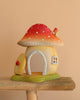 The Bumbu Wooden Toadstool House features a whimsical red and white ceramic mushroom design with a round door and window, set on sustainably sourced wood for an enchanting playset shown against a beige background.