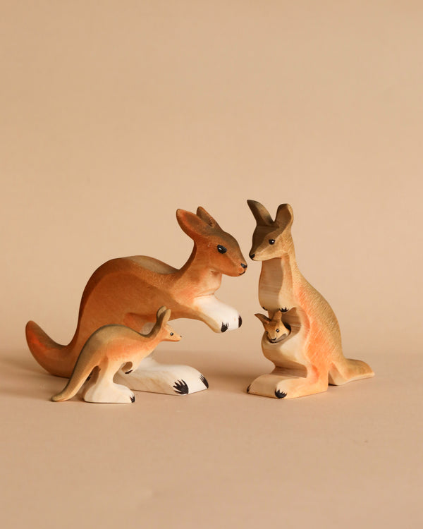 Three kangaroo figurines from the Bumbu Wooden Kangaroo Family Set, crafted from sustainably sourced wood, are arranged on a beige background—two adults face each other while a smaller kangaroo stands in front, inspiring imaginative play.