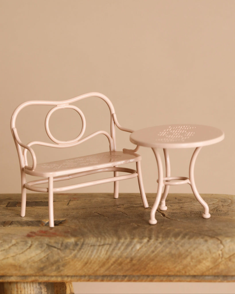 The Maileg Outdoor Tea Set, in pastel pink, sits on a rustic wooden surface against a beige background. This charming miniature set is perfect for your Maileg big sister mouse or other tiny friends.