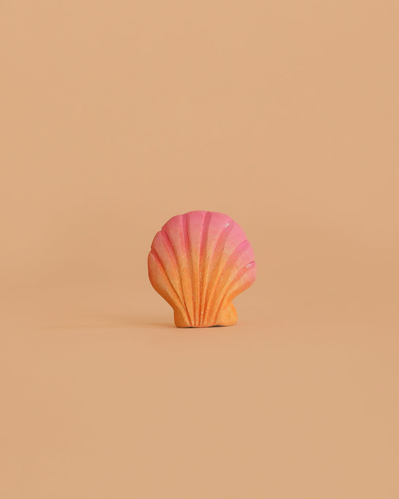 The Bumbu Handmade Wooden Pink Seashell, a small Montessori-inspired toy with an orange-to-pink gradient, is centered on a plain beige background.