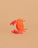 A handmade orange and pink crab with white dots from the Bumbu Wooden Ocean Set is centered on a plain beige background.