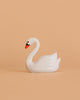 The Bumbu Handmade Wooden Swan, a small handcrafted toy with an orange beak, is displayed against a plain peach-colored background.