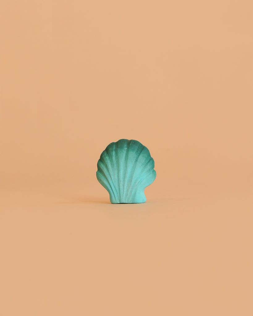 A turquoise seashell stands upright against a plain peach background, capturing the charm of the Bumbu Handmade Wooden Ocean Set.