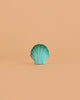 A handmade Bumbu Wooden Green Seashell is centered on a simple peach background, highlighting its Montessori-inspired design.
