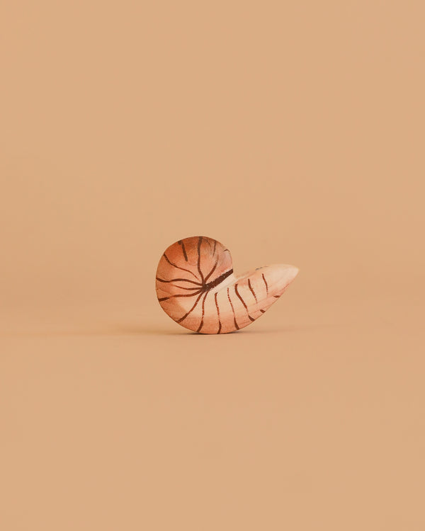 The Bumbu Handmade Wooden Spiral Shell, featuring dark stripes, stands upright on a plain peach background. This minimalist and eco-friendly Montessori toy is centered in the image with no other objects present.