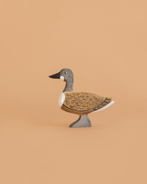 The Bumbu Handmade Wooden Wild Goose is a small, handcrafted wooden toy painted in brown, gray, black, and white and stands on a plain light tan background.