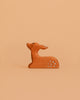 A small, minimalist ceramic deer with white spots sits against a light orange background, ideal for pairing with the Bumbu Handmade Wooden Woodland Animals Set in any eco-friendly decor.