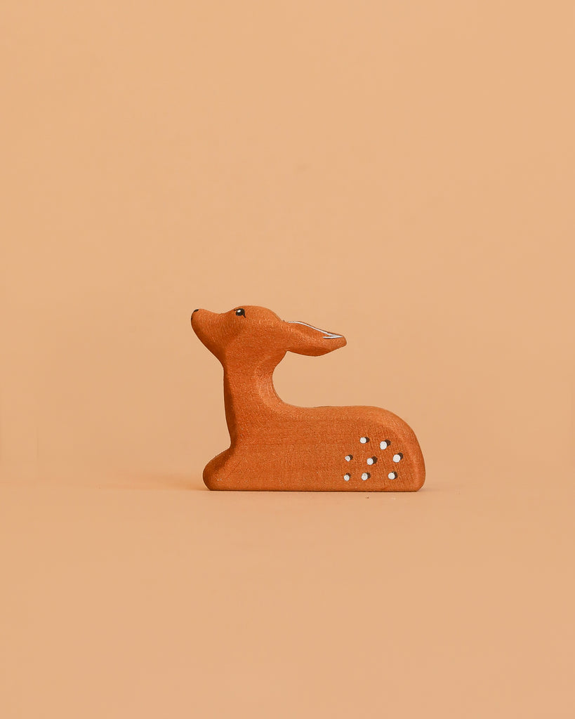 A small, minimalist ceramic deer with white spots sits against a light orange background, ideal for pairing with the Bumbu Handmade Wooden Woodland Animals Set in any eco-friendly decor.